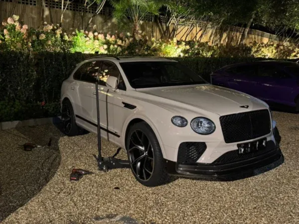 White Bentley SUV raised on a jack during a nighttime mobile tyre service, with fitting tools beside the vehicle.