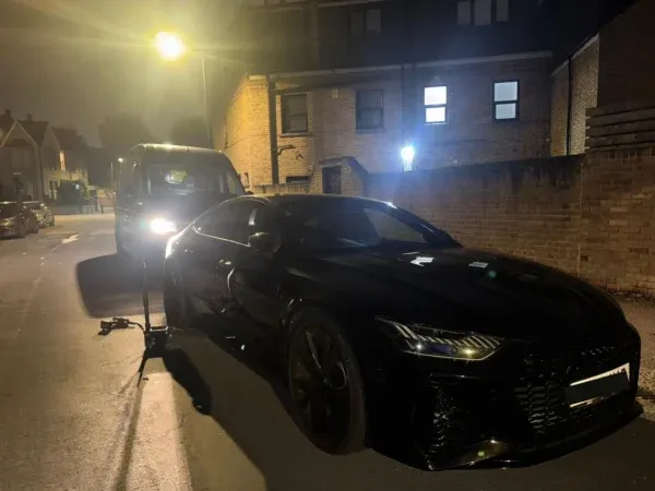 Black Audi receiving nighttime mobile tyre service on a residential street, with a service van and fitting equipment behind the car.