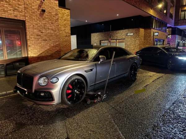 Grey Bentley being serviced at night during a mobile tyre fitting callout, with a jack and tools positioned beside the front wheel.
