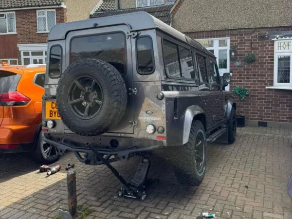 Land Rover Defender raised on a jack during a mobile tyre service outside a residential property.
