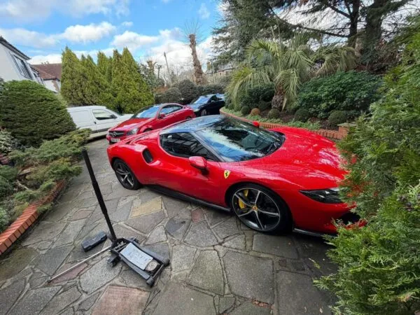 Red Ferrari parked on a driveway during mobile tyre service, with a hydraulic jack and fitting tools beside the car.