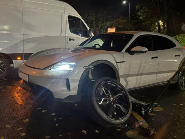 White Porsche SUV raised on a jack during a nighttime mobile tyre change, with the front wheel removed beside the vehicle.